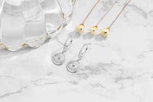 Detailed view of S925 sterling silver evil eye hoop earrings with zircon on marble surface