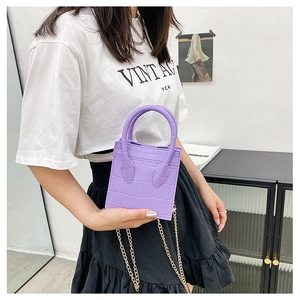 Close-up of a purple crocodile pattern mini bag with golden chain strap on a model