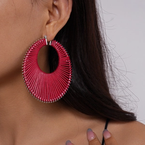 Close-up of fuchsia woven round hoop earring with intricate thread and metallic bead details