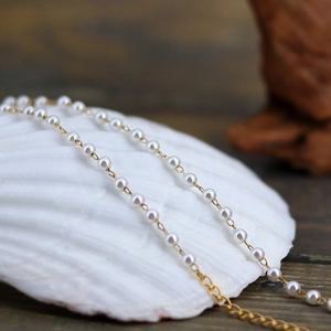 Elegant French style pearl necklace with gold chain draped on a white shell prop