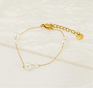 Detail of gold stainless steel pearl bracelet featuring elegant chain on ripple surface
