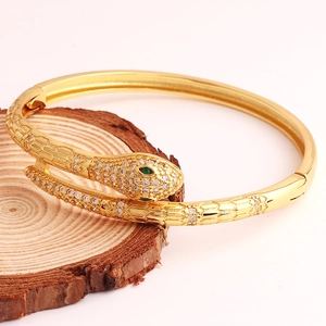 Detail of gold snake bracelet with white cubic zirconia and green gemstone eyes
