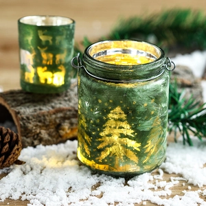 Christmas green glass candle holders with reindeer patterns and metal handle on snowy wood