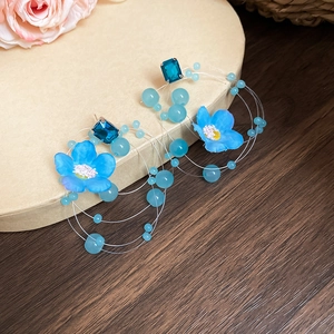 Close-up of blue fabric flower earrings with tassel beads and square crystal accents