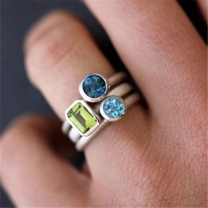 Detail of stacked matte silver rings with emerald cut green and blue zircon stones