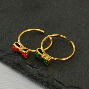 Detail of gold bow rings with red and green micro-pave crystals on dark stone