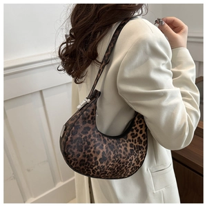 Leopard print crescent hobo bag shown as a shoulder bag on a model in beige suit