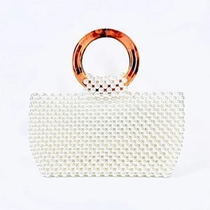 Detail of handmade pearl beaded handbag featuring round amber resin ring handles
