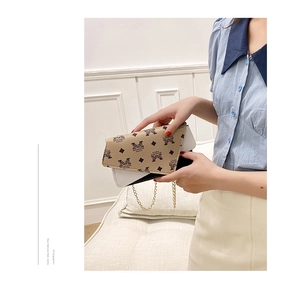 Macro shot of a model holding a chain crossbody bag with beige monogram pattern