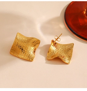 Macro detail of gold irregular wave earrings with brushed and hammered metal textures