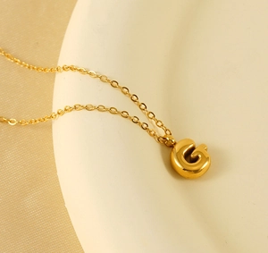 Detail of 18K gold bubble letter G pendant on thin chain over elegant background