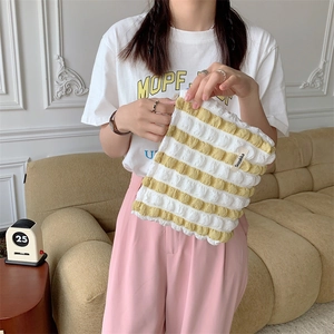 Detail of yellow striped bubble cloud cosmetic bag with brand tag held by model