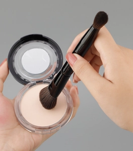 Detail showing dual-ended makeup brush application with compact powder and built-in mirror