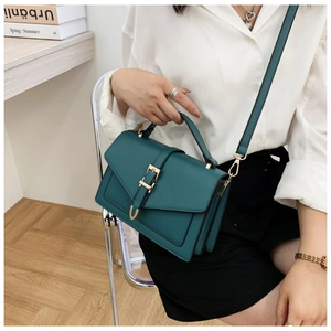 Model wearing dark green leather crossbody bag with metal buckle and adjustable strap