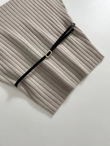 Detailed macro shot of oatmeal knit fabric texture featuring a slim black belt with gold buckle