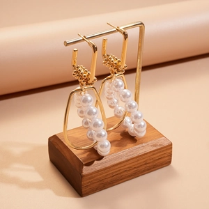 Detailed macro view of geometric gold metal earrings with faux pearl trapezoid pendant