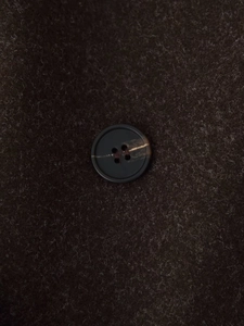 Detailed close-up of a classic four-hole button on thick dark brown wool fabric