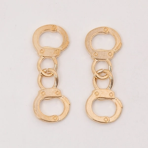 Detailed view of creative gold-tone handcuff-shaped alloy jewelry charms on a white surface