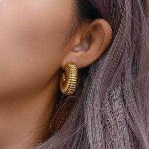 Detail of chunky gold ribbed hoop earring worn on model showing thick hollow texture