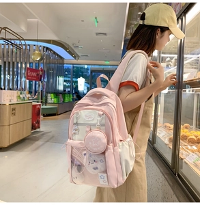 Girl wearing a pink and cream student backpack with transparent pocket and charms