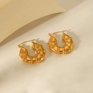 Golden bamboo hollow hoop earrings in chunky croissant style on beige background