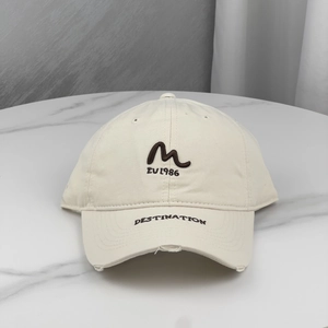 Detail of embroidered 'M' patch and DESTINATION text on distressed beige baseball cap