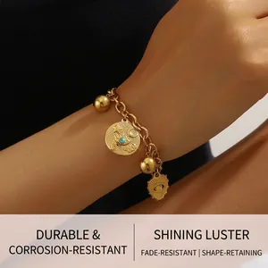 Close-up of a gold link bracelet featuring evil eye, heart, and ball charms on a wrist