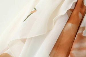 Detail of floral chiffon fabric with orange prints and fine machine-stitched edges