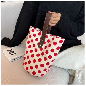 Polka dot canvas bucket bag with brown leather handles held on a cream sofa