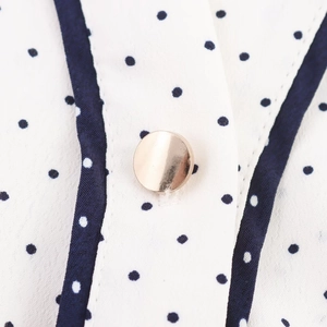 Détail macro d'une robe chemise à pois avec boutons dorés et texture de tissu fine