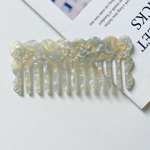 Detail of wide-tooth marble acetate comb with blue and beige wavy edge design