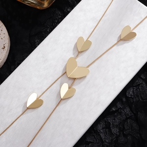 Close-up of gold snake chain necklace with five 3D folded heart charms on stone surface