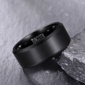 Brushed black tungsten carbide ring for men leaning against a textured grey rock background