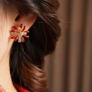 Detailed close-up of a red flower earring with sparkling zircons worn by a female model
