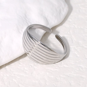 Détail macro d'une bague ouverte argentée avec texture rainurée sur un support en pierre