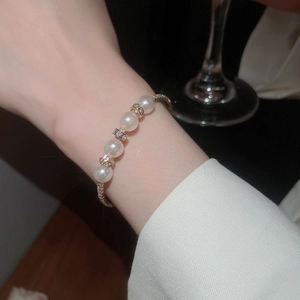 Detailed shot of layered pearl bracelet with diamond-set beads on elegant gold-woven chain