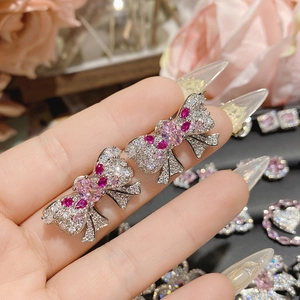 Macro detail of bow-shaped earring with pink gemstone and 18K gold plating