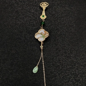 Détail de broche fleur aux pétales blancs, perle et long gland sur fond en tissu noir