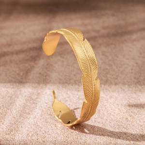 Detailed view of 18K gold plated stainless steel feather cuff bracelet on sandy texture