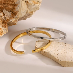 Minimalistische polierte Edelstahl-Armreifen in Gold und Silber auf einem Stein