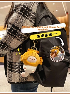 Detail of yellow plush cat keychain with squeaky feature and golden clasp on a bag