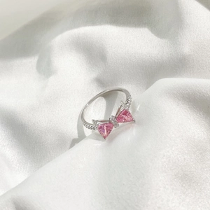 Detail of s925 silver ring featuring pink heart bow design on white silk background