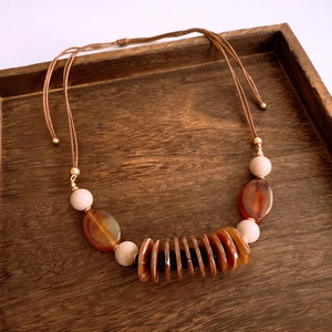 Detail of bohemian necklace with leather cord, amber beads, and striped disc pendant