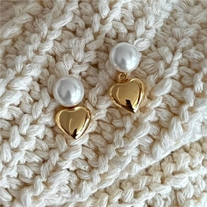 Macro shot of gold heart dangle earrings with white pearls on a soft knit background