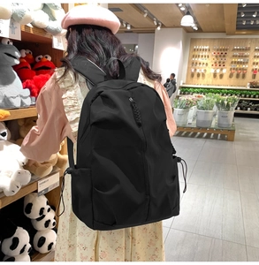 Detail of minimalist black nylon backpack featuring vertical front zipper and side drawstring pocket