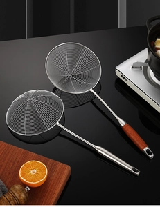 Detail view of two stainless steel skimmers with wooden handles on black kitchen counter
