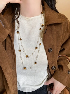 Gros plan d'un collier double épaisseur avec œil de tigre et perles sur veste en daim