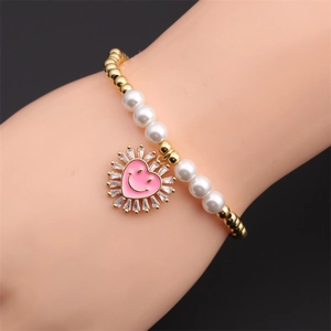 Dettaglio di un bracciale con sfere dorate, perle e un ciondolo a cuore rosa sorridente