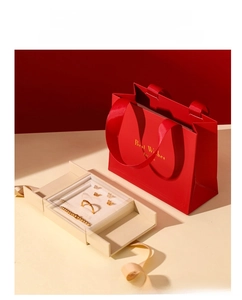 Close-up of red gift bag and cream drawer jewelry box with smooth satin texture