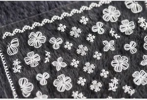 Macro shot of 3D embossed white floral nail art stickers with lace patterns on dark plush background
